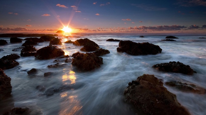 Sunset over rocky ocean shore with waves