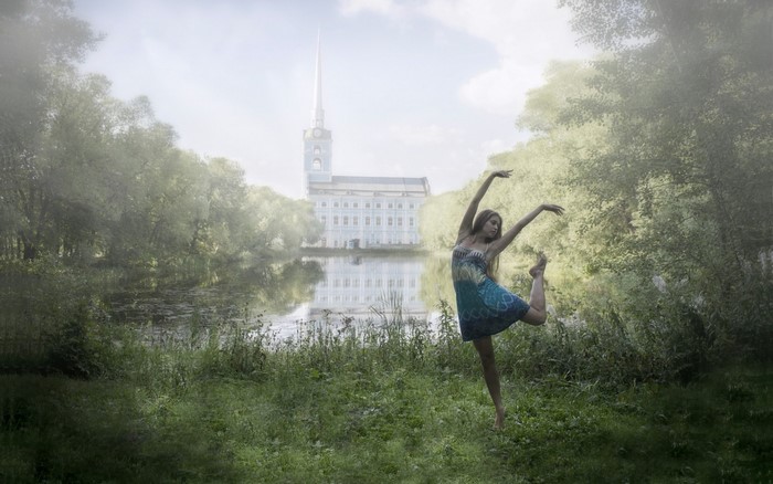 Woman dancing by a lake with a building in the background