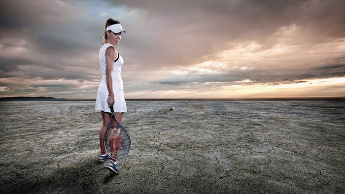 Woman in tennis outfit on cracked earth with dramatic sky