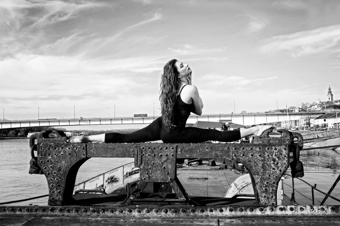 Woman performing a split on a metal structure by the water