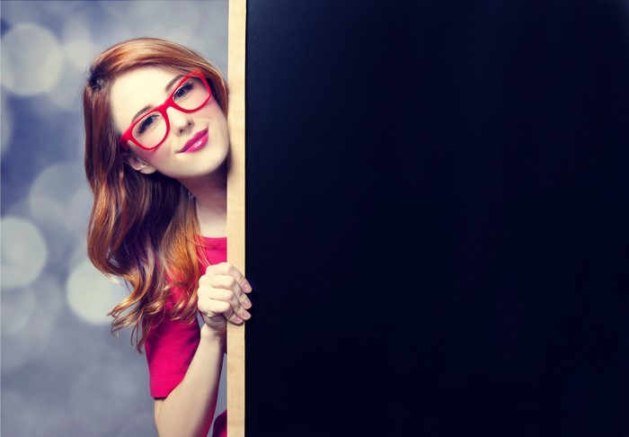 Woman with red glasses peeking from behind a blackboard