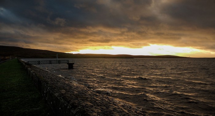 Sunset over a reservoir with a pier and stone embankment