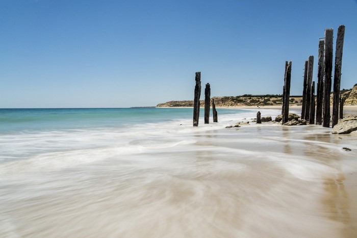 Wooden pier remnants on a sandy beach with ocean waves