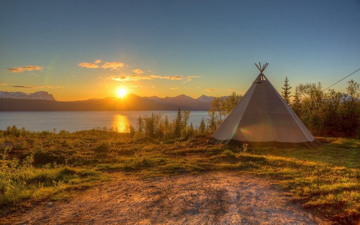 Tipi by a lake at sunset with mountains