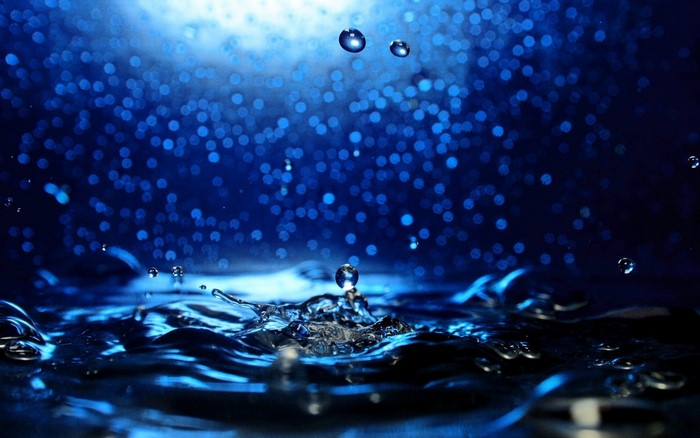 Water drops falling into dark blue water with bokeh lights