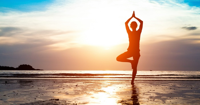 Silhouette of a woman doing yoga on a beach at sunset