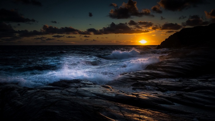 Sunset over stormy ocean waves crashing on rocky shore