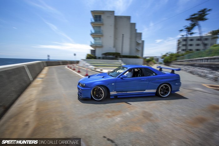 Blue Nissan Skyline R34 GT-R driving on coastal road