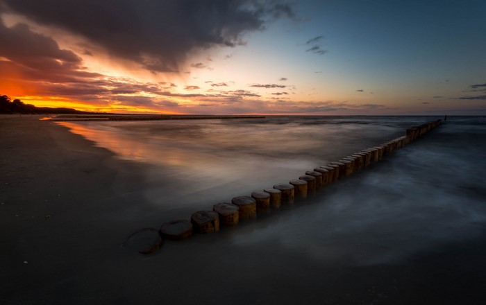 Sunset over the sea with wooden breakwaters on the shore