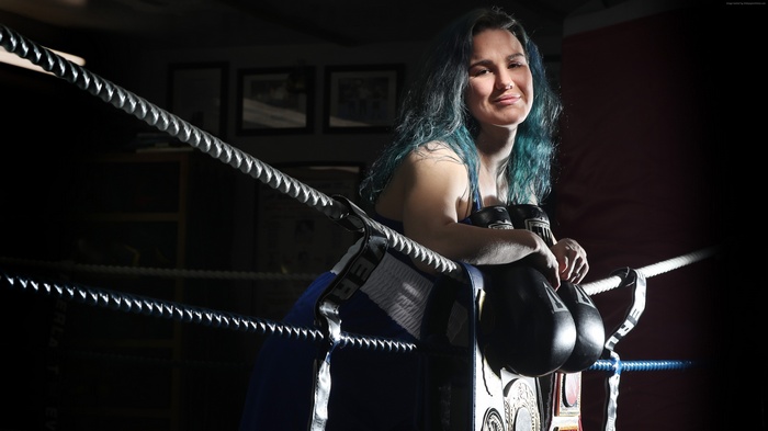 Woman boxer with championship belt and gloves in ring