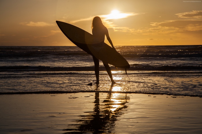 Silhouette of a surfer with a surfboard at sunset
