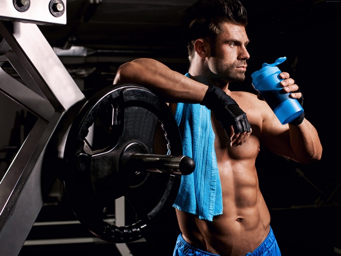 Man drinking from a shaker bottle in a gym