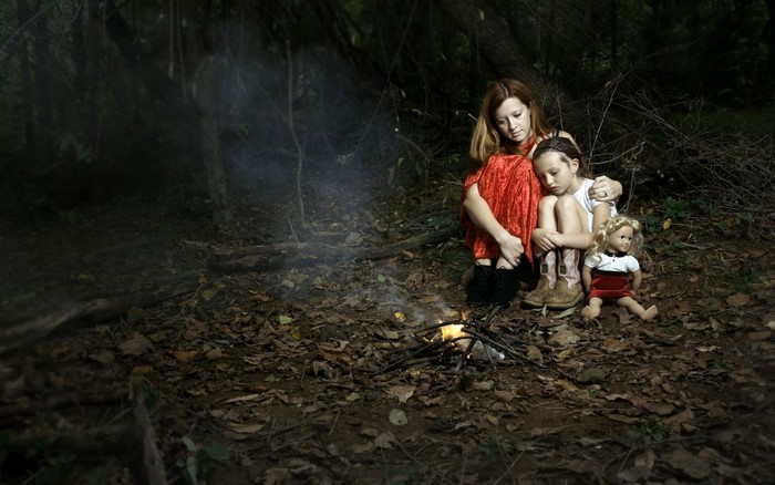 Woman and child with doll by campfire in forest