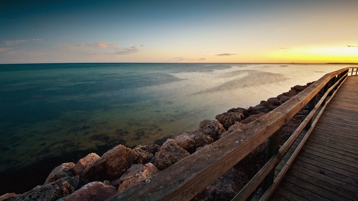 Wooden boardwalk along a rocky shore at sunset