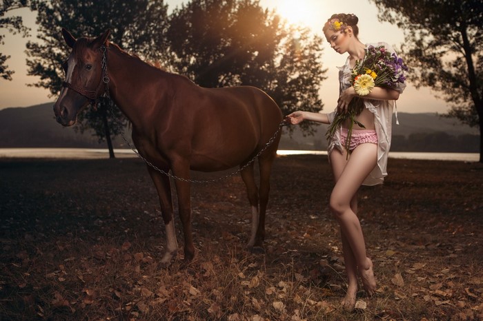 Woman with flowers and horse by lake at sunset