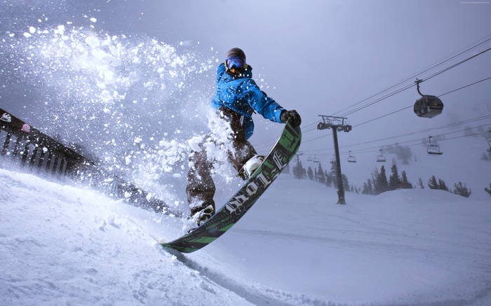 Snowboarder jumping in the snow with ski lift in background