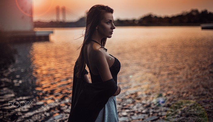 Woman in black dress by the water at sunset
