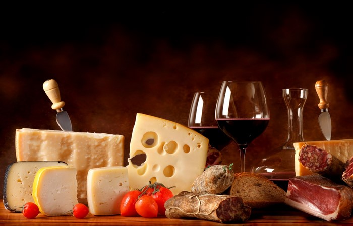 Still life of cheese, cured meats, bread, tomatoes, and red wine