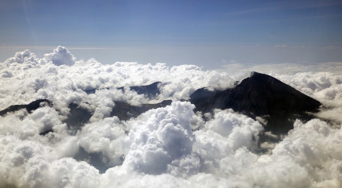 Mountain peaks emerging from clouds under a blue sky
