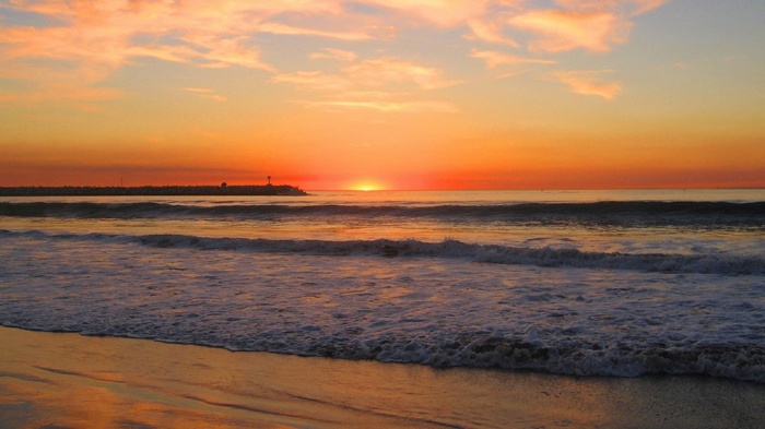 Sunset over the ocean with waves and a distant pier