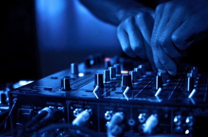 DJ hands mixing music on a blue-lit console