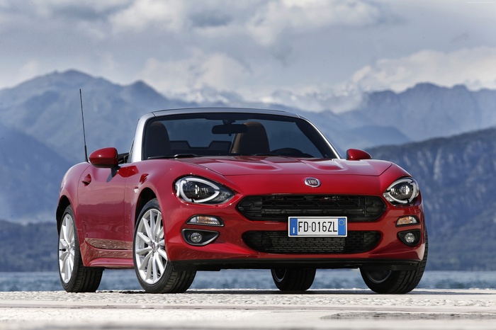 Red Fiat 124 Spider convertible parked by mountains