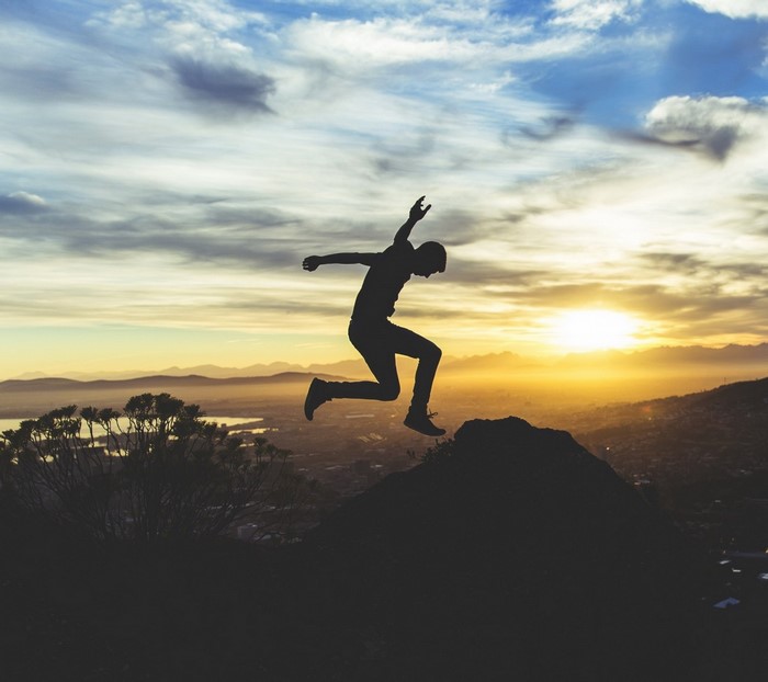 Silhouette of a man jumping over a rock at sunset