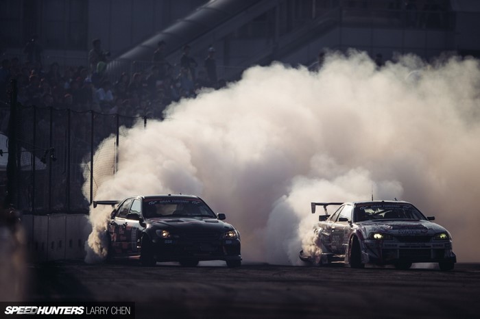 Two cars drifting in smoke with spectators