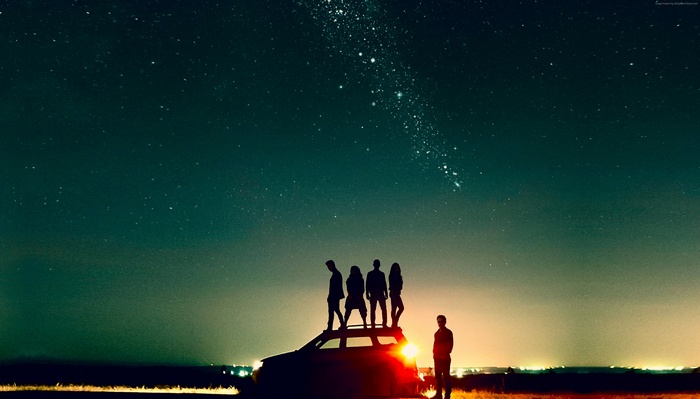 Silhouettes of people on a car under the stars