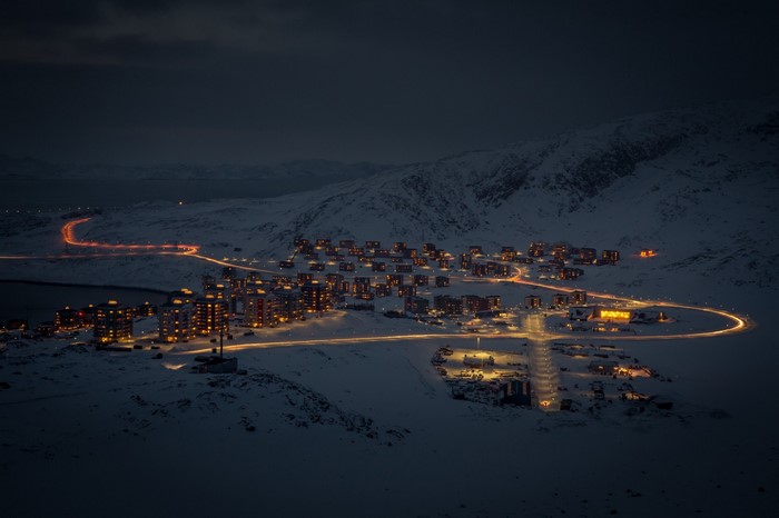 Snowy town at night with illuminated buildings and car lights