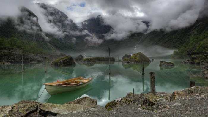Boat on a misty lake with mountains and clouds