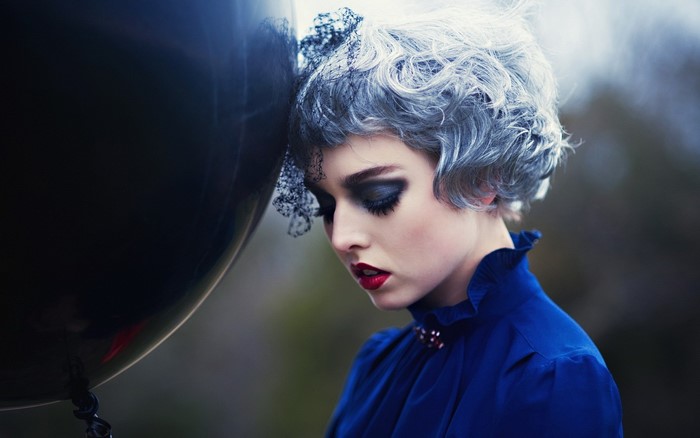 Woman with dramatic makeup and blue dress holding a balloon