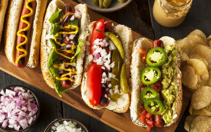 Four gourmet hot dogs with various toppings and sides