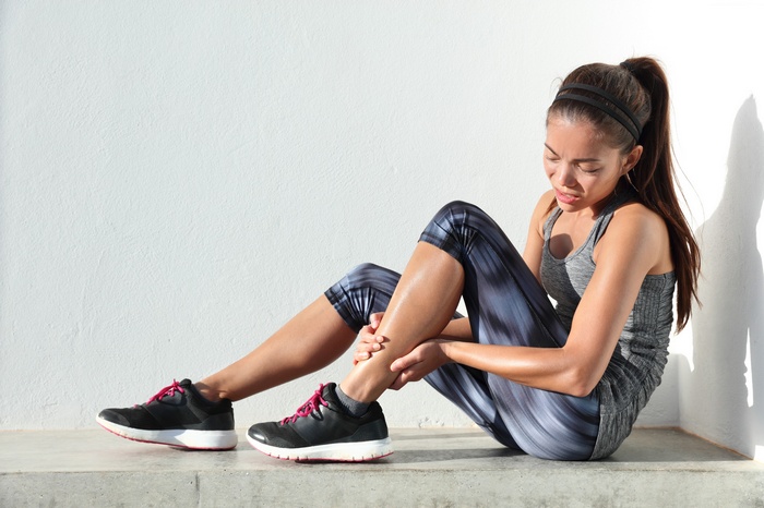 Woman in sportswear holding her injured leg