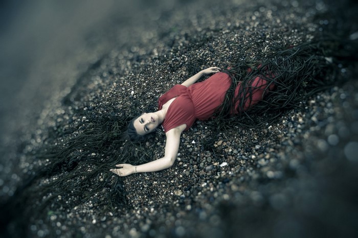 Woman in red dress lying on a beach with seaweed