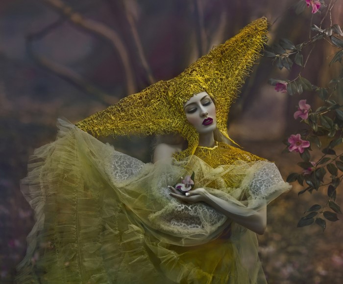 Woman in elaborate yellow headdress and gown holding a flower