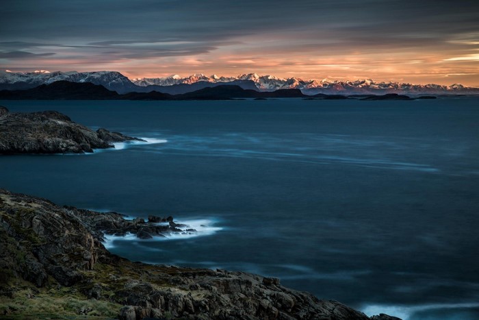 Sunset over a rocky coast with snow-capped mountains