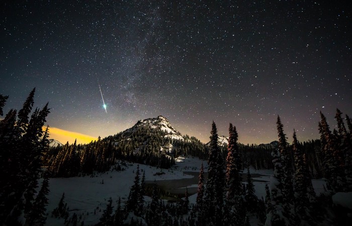 Meteor shower over snow-covered mountains and pine trees at night