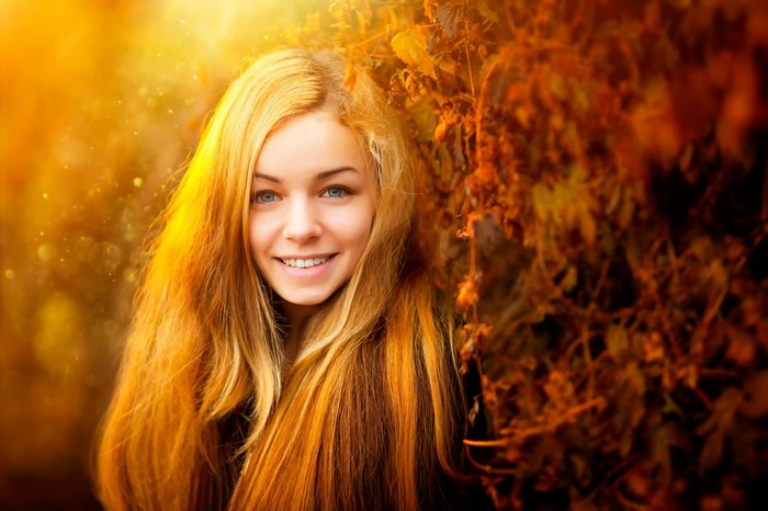 Young woman with long blonde hair smiling outdoors in autumn