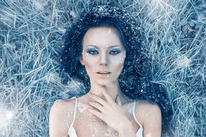Woman with snow and blue makeup lying in grass