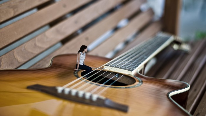 Woman sitting on a miniature guitar on a wooden bench