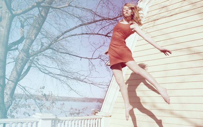 Woman in orange dress jumping near a house