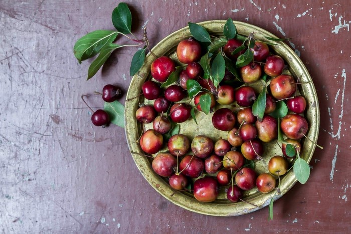 Small red apples and cherries on a brass plate