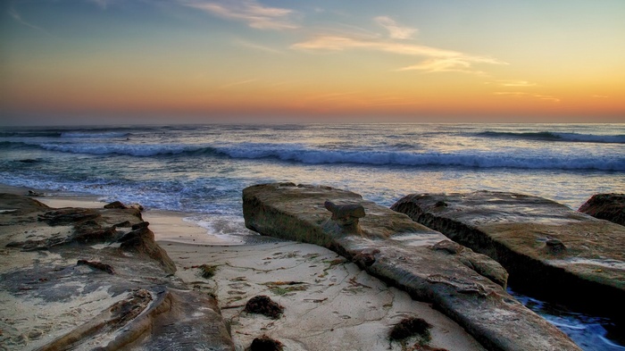 Ocean waves crash on a rocky beach at sunset