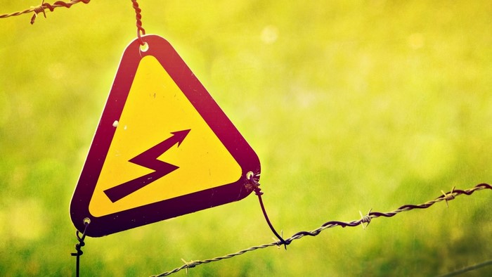 Yellow danger sign with lightning bolt on barbed wire
