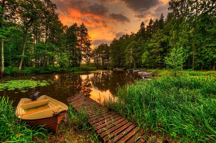 Boat docked by a lake at sunset with forest reflection