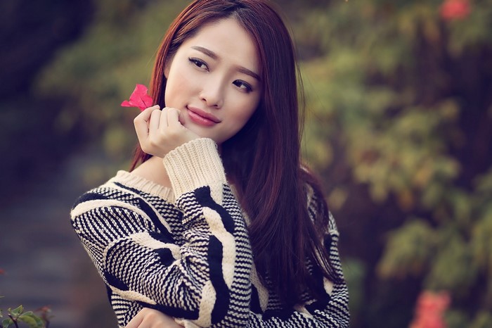 Asian woman with long brown hair holding a pink flower