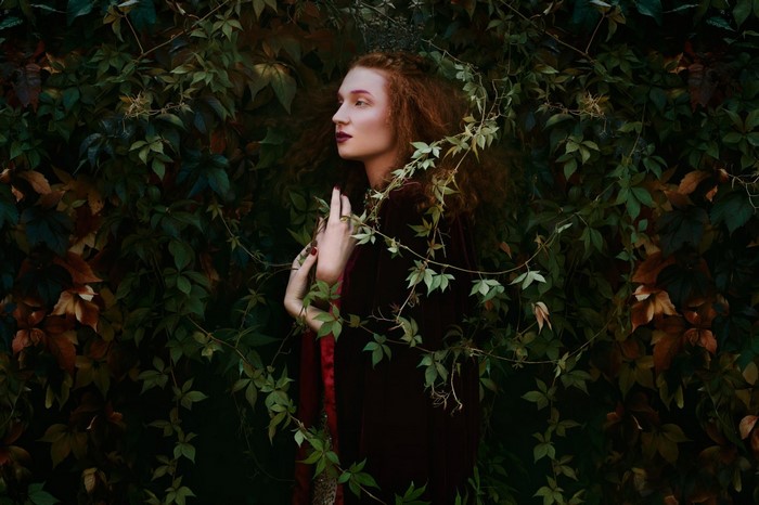 Woman with red hair in a dark dress surrounded by foliage