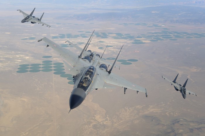Three Sukhoi Su-30MKI fighter jets in flight over circular fields