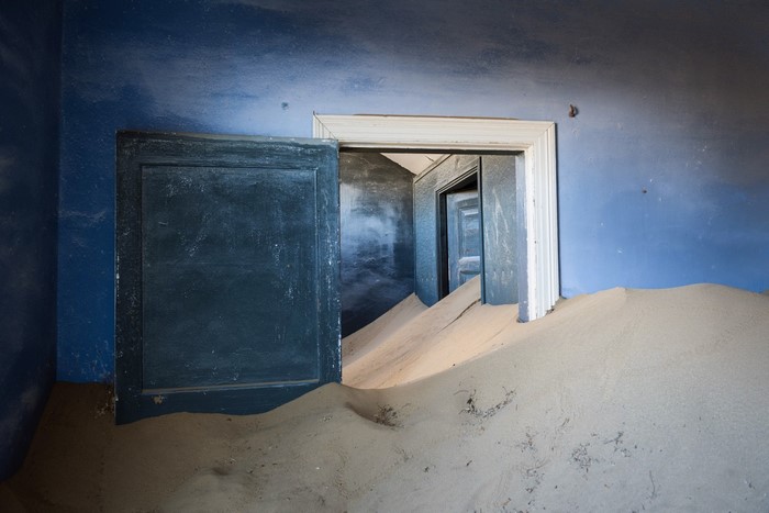 Abandoned room filled with sand, blue walls, open doors